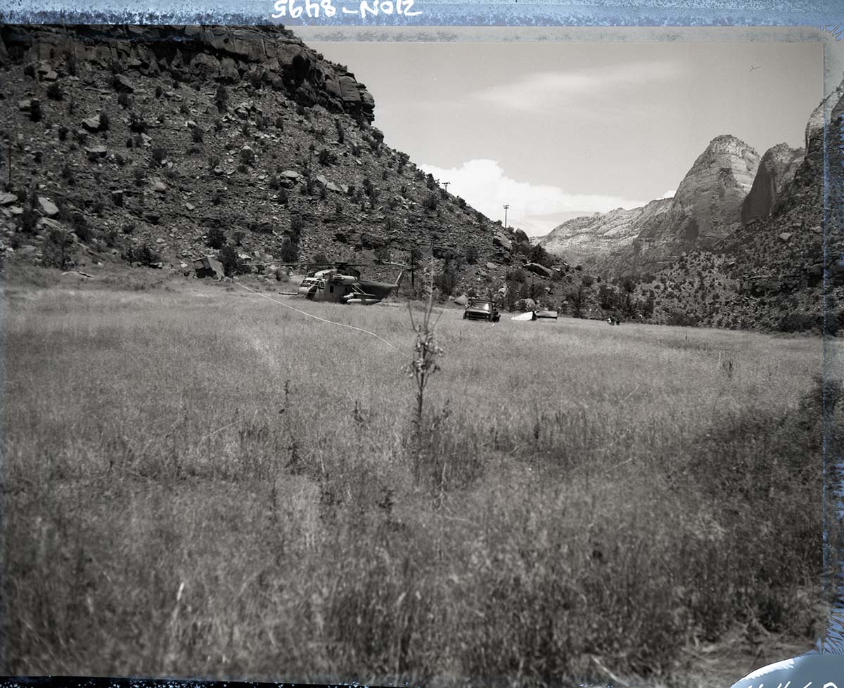 Pilot module from F-111 aircraft that crashed behind Zion Lodge July 11, 1973 helicopter and truck from Nellis Air Force Base loading module near field in front of Visitor Center.