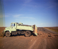 Color Photo of a damaged dump truck- tailgate and side ripped open.