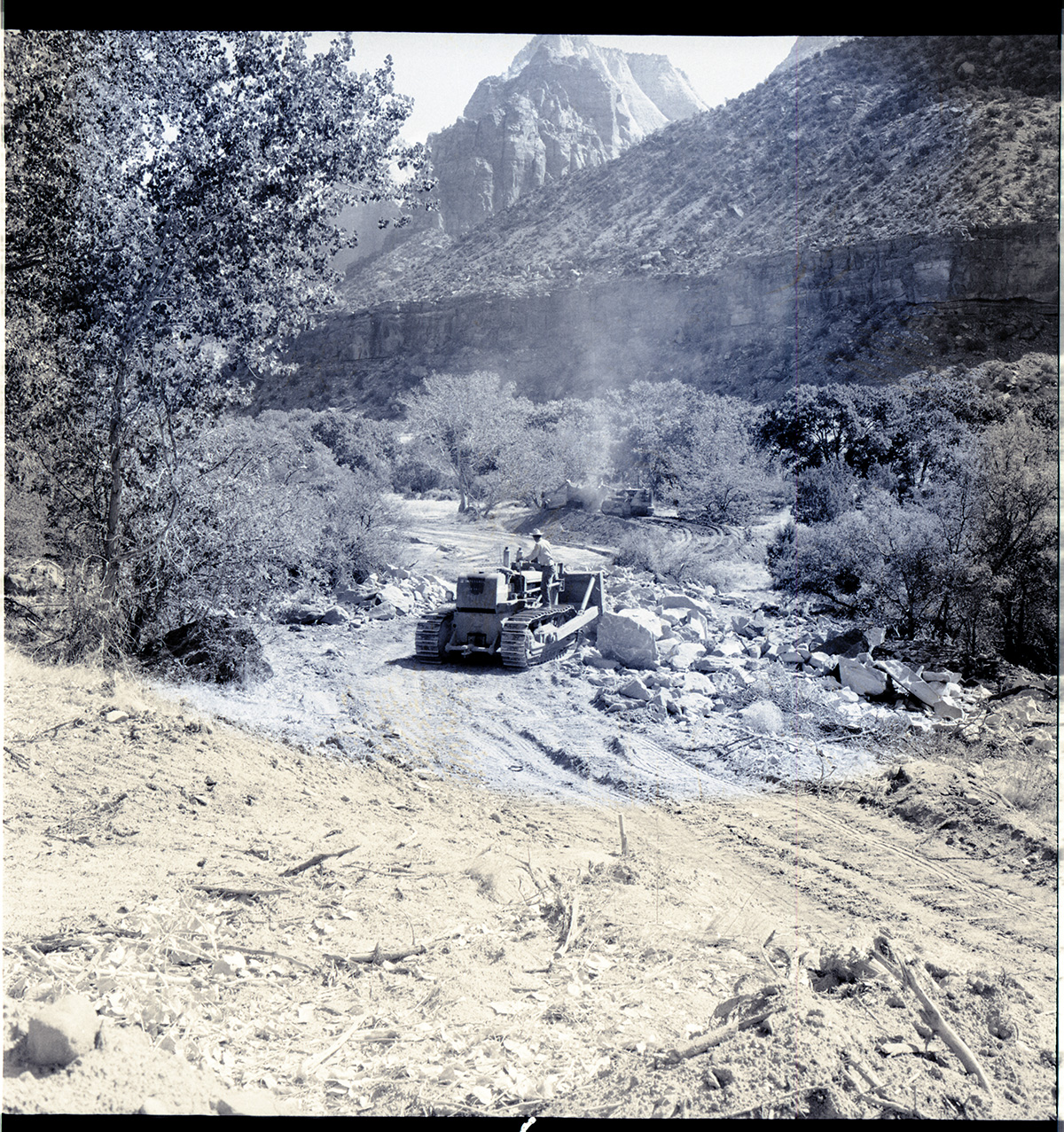 Clearing the right-of-way for new highway, from South Entrance Station to Virgin River Bridge. Bulldozer clearing and scraper collecting top soil (in background).