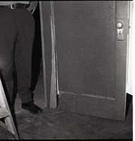 Damage to door in men's dorm at Zion Lodge. Superintendent Robert C. Heyder standing in doorway.